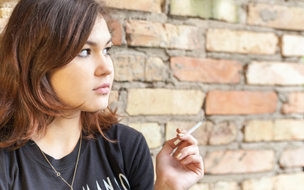 Jugendliche mit Zigarette vor einer Backsteinwand
