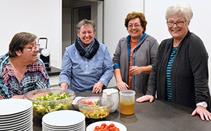 Vier Personen stehen vor einer Theke mit Essen und lachen