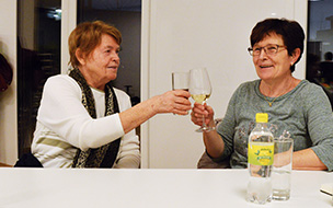 Zwei Frauen sitzen an einem Tisch und stossen mit Gläsern an