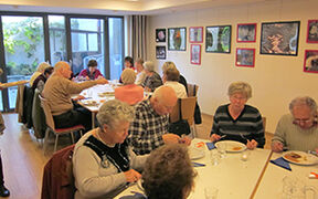 Mehrere ältere Personen sitzen an mehreren Tischen und essen
