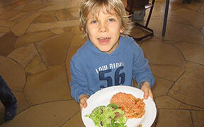 Lachends Kind zeigt einen Teller mit einer Mahlzeit